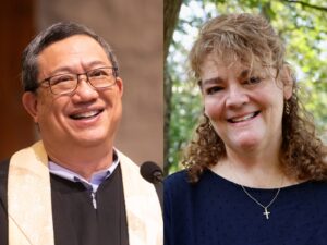 A man on the left in a clergy robe and glasses smiles, and on the right a woman with curly hair and a cross on her necklace smiles, with greenery behind her.