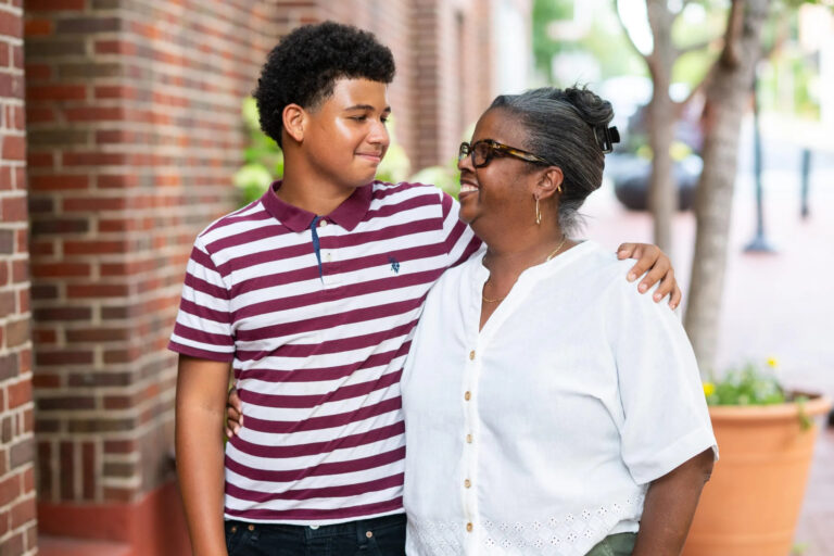 A boy in a striped, buttoned polo embraces a woman with graying hair.